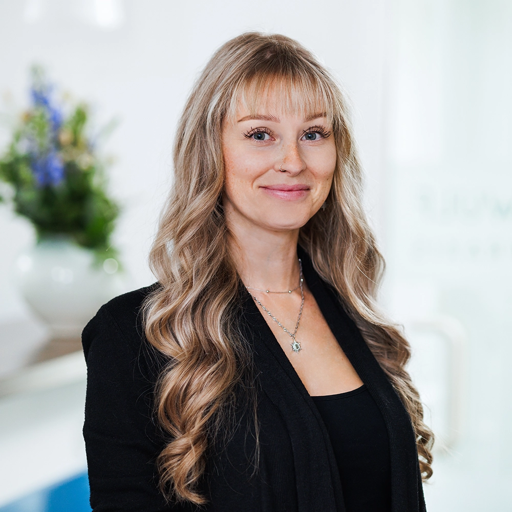 Portrait Praxisteam Janet Mitarbeiterin Janet mit langen blonden Haaren lächelt freundlich vor hellem Praxishintergrund